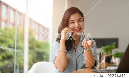Young working woman having phone conversation with her business partner while sitting in bright modern office Young working woman having phone conversation with her business partner while sitting in bright modern office 92278855