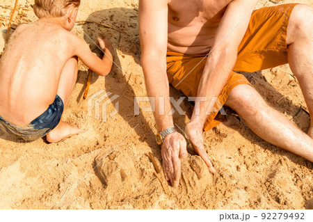 a father with vitiligo and his son play with sand on the beach on a hot summer day. Building castles. Without faces. The concept of a beach holiday. 92279492