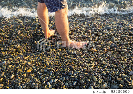 man walking alone on the pebble beach in the sunset 92280609