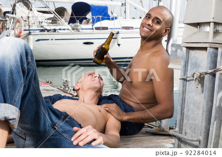 two guys without shirts in jeans sitting and relaxing near yachts in the port two guys without shirts in jeans sitting and relaxing near yachts in the port 92284014