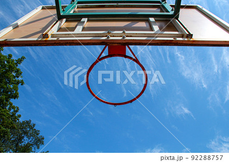 Basketball ring on the background a blue sky with white clouds and green tree. Basketball hoop on a shield on an outdoor sports ground. Basketball equipment. Copy space Basketball ring on the background a blue sky with white clouds and green tree. Basketball hoop on a shield on an outdoor sports ground. Basketball equipment. Copy space 92288757