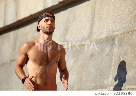 Urban sports. Sporty man shirtless jogging for fitness in the city park on a beautiful summer day Urban sports. Sporty man shirtless jogging for fitness in the city park on a beautiful summer day 92295390