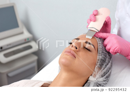 Beautiful woman receiving ultrasound cavitation facial peeling. Cosmetology and facial skin care Beautiful woman receiving ultrasound cavitation facial peeling. Cosmetology and facial skin care 92295432