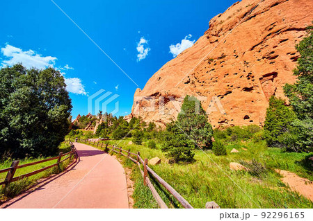 Paved walking path with fence through desert with large red mountain pillars Paved walking path with fence through desert with large red mountain pillars 92296165