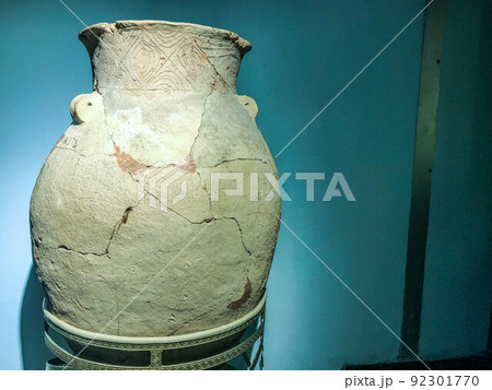 ancient clay vase with cracks. Museum piece. vase with hand-painted top and large cracks. interior vase against a blue matte wall ancient clay vase with cracks. Museum piece. vase with hand-painted top and large cracks. interior vase against a blue matte wall 92301770