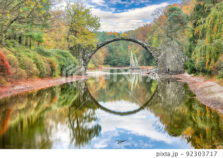 Astonishing autumn landscape in Azalea and Rhododendron Park Kromlau. Rakotz Bridge (Rakotzbrucke, Devil's Bridge) Astonishing autumn landscape in Azalea and Rhododendron Park Kromlau. Rakotz Bridge (Rakotzbrucke, Devil's Bridge) 92303717