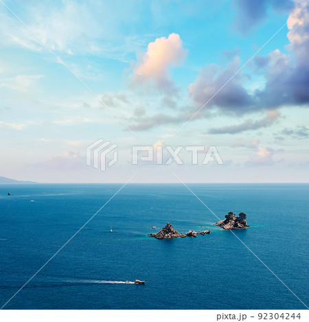 Picturesque view on rocks on a sunny day from the sea. Budva riviera, Montenegro. Aerial view of Sveti Nikola, Budva island, Montenegro. Hawaii beach, umbrellas and bathers and crystal clear waters 92304244