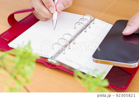 スマホを見ながら手帳を書き込む人の手元 92305821