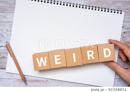 「WEIRD」と書かれたブロック、ノート、ペン、手 92308651