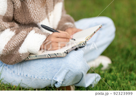 Girl writing notes with pen while sitting in the street. 92323999