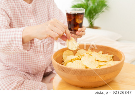 寝室でコーラを飲みながらポテトチップスを食べるミドル女性 92326847