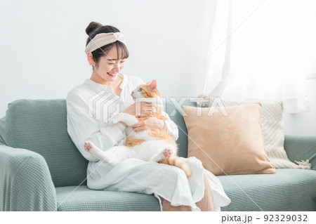 家で猫を抱っこする日本人女性（ペット・飼い主） 92329032