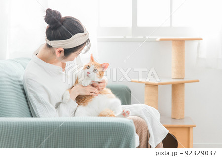 家で猫を抱っこする日本人女性（ペット・飼い主・キャットタワー） 92329037