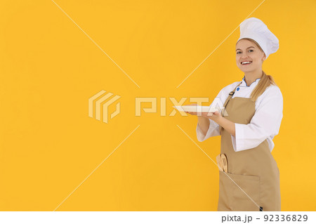 Young female chef in uniform on yellow background 92336829