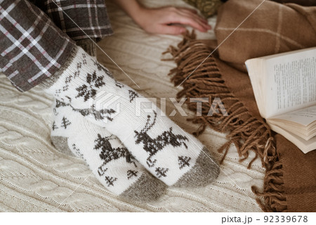 Woman in warm woolen knitted socks sits on sofa near opened book Woman in warm woolen knitted socks sits on sofa near opened book 92339678
