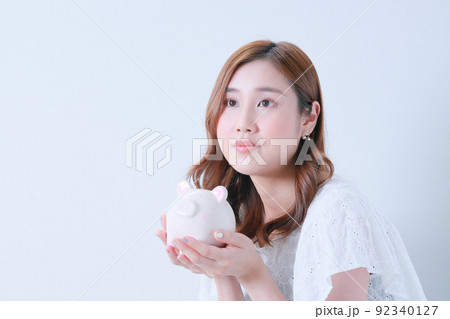 両手で豚の貯金箱を持つ若い女性 両手で豚の貯金箱を持つ若い女性 92340127