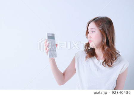 電卓を見つめるTシャツ姿の若い女性 92340486