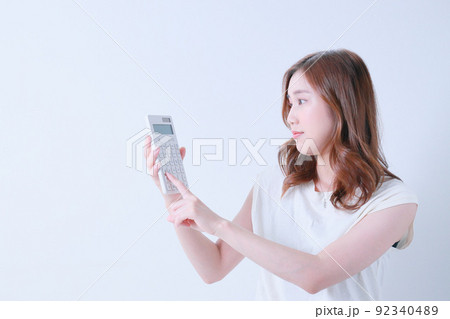 白色の電卓で計算をする若い女性 白色の電卓で計算をする若い女性 92340489