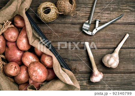 Raw whole washed organic potatoes and garlic on sackcloth over old wooden plank background. Top view with space. Close up 92340799