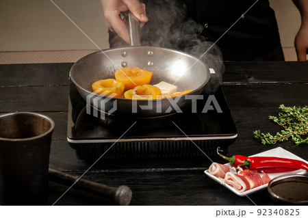Peaches on a fry pan. Canned fruit yellow peaches, black wooden background, board. 92340825
