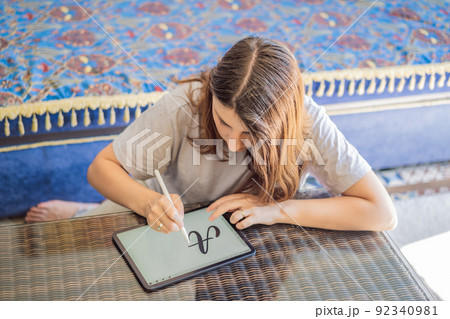 Calligrapher Young Woman writes phrase on digital tablet. Inscribing ornamental decorated letters. Calligraphy, graphic design, lettering, handwriting, creation 92340981