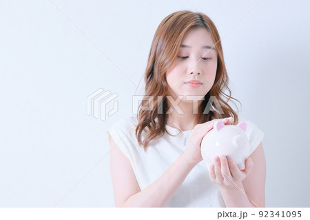 ブタの貯金箱を撫でる白いTシャツ姿の女性 92341095