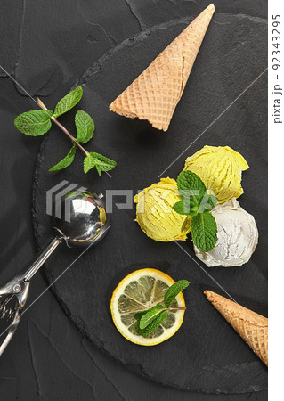 Tasty creamy and lemon ice cream decorated with mint served on a stone slate over a black background. 92343295