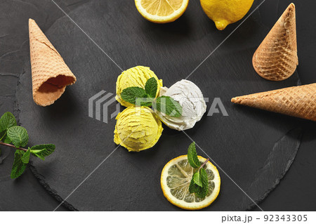Tasty creamy and lemon ice cream decorated with mint served on a stone slate over a black background. Tasty creamy and lemon ice cream decorated with mint served on a stone slate over a black background. 92343305