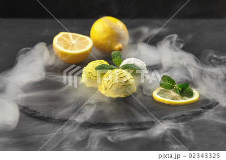 Tasty creamy and citrus lemon ice cream decorated with mint served on a stone slate over a black background. Tasty creamy and citrus lemon ice cream decorated with mint served on a stone slate over a black background. 92343325