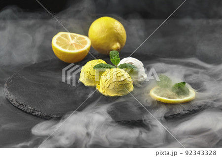 Tasty creamy and citrus lemon ice cream decorated with mint served on a stone slate over a black background. 92343328