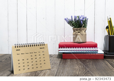 Brown March 2023 calendar on wooden desk with office stationery. 92343473