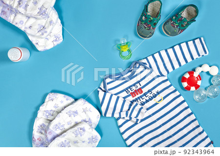 Babies goods: cloth diaper, baby powder, nibbler, cream, teether, soother, baby toy on blue background. Copy space. Top view. Babies goods: cloth diaper, baby powder, nibbler, cream, teether, soother, baby toy on blue background. Copy space. Top view. 92343964