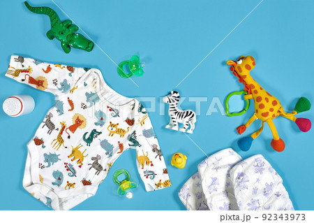 Babies goods: cloth diaper, baby powder, nibbler, cream, teether, soother, baby toy on blue background. Copy space. Top view. Babies goods: cloth diaper, baby powder, nibbler, cream, teether, soother, baby toy on blue background. Copy space. Top view. 92343973