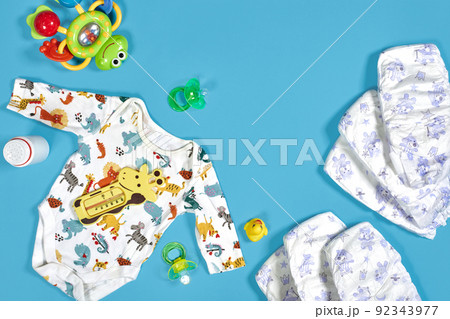 Babies goods: cloth diaper, baby powder, nibbler, cream, teether, soother, baby toy on blue background. Copy space. Top view. Babies goods: cloth diaper, baby powder, nibbler, cream, teether, soother, baby toy on blue background. Copy space. Top view. 92343977