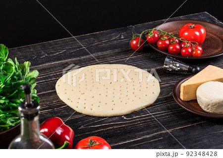 Raw dough for pizza preparation with ingredient: tomato sauce, mozzarella, tomatoes, basil, olive oil, cheese, spices served on rustic wooden table. Raw dough for pizza preparation with ingredient: tomato sauce, mozzarella, tomatoes, basil, olive oil, cheese, spices served on rustic wooden table. 92348428