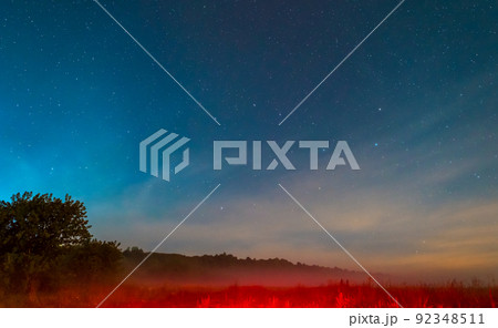 The night sky with many bright stars over the forest and the field with a red glow. A nighttime abstract landscape. The night sky with many bright stars over the forest and the field with a red glow. A nighttime abstract landscape. 92348511