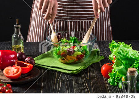 Man preparing salad with fresh vegetables on a wooden table. Cooking tasty and healthy food Man preparing salad with fresh vegetables on a wooden table. Cooking tasty and healthy food 92348708