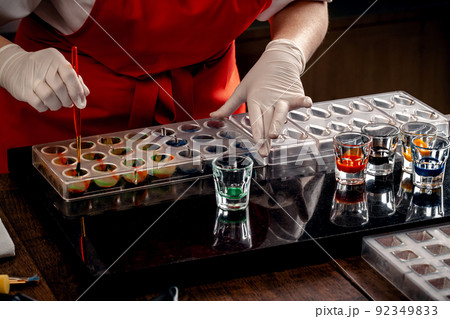Woman a confectioner in red uniform and white gloves doing candy in special shapes from dairy chocolate with edible paint. Woman a confectioner in red uniform and white gloves doing candy in special shapes from dairy chocolate with edible paint. 92349833