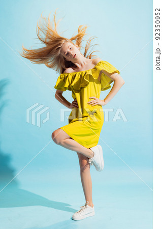 Studio shot of young beautiful blonde in summer yellow dress isolated on light blue background. Concept of beauty, art, fashion, human emotions 92350952