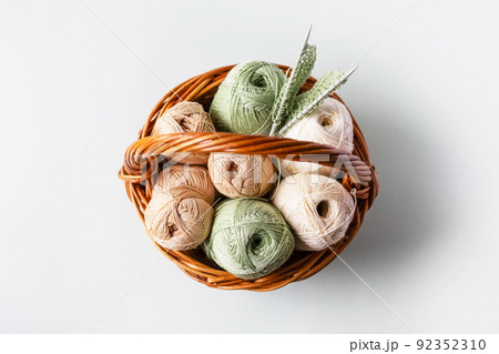 Green and brown yarn threads in a basket for knitting warm clothes with knitting needles on a white background, knitting hobby, flat lay Green and brown yarn threads in a basket for knitting warm clothes with knitting needles on a white background, knitting hobby, flat lay 92352310