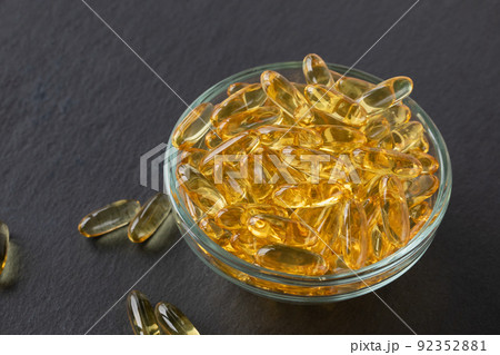 Cod liver fish oil capsules in glass bowl on black slate plate background. Omega 3, Vitamin E supplements. Healthy diet concept. Close-up, copy space Cod liver fish oil capsules in glass bowl on black slate plate background. Omega 3, Vitamin E supplements. Healthy diet concept. Close-up, copy space 92352881
