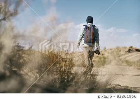 rear view of male asian photographer with backpack walking on dirt road in gobi desert rear view of male asian photographer with backpack walking on dirt road in gobi desert 92361956