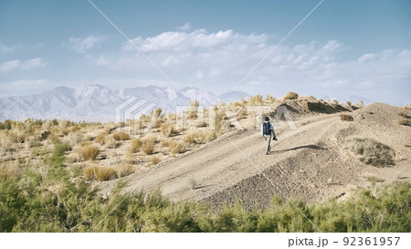 rear view of an asian man backpacker photographer walking on a dirt road through gobi desert 92361957