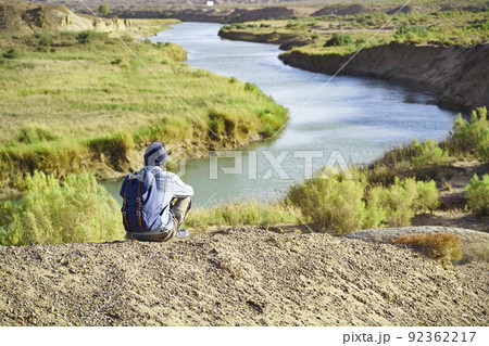 rear view of male asian photographer sitting on top of a hill looking down at a river rear view of male asian photographer sitting on top of a hill looking down at a river 92362217
