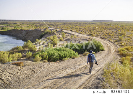 asian man photographer walking on dirt road in gobi desert looking at landscape at sunset asian man photographer walking on dirt road in gobi desert looking at landscape at sunset 92362431