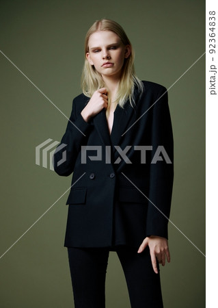 A blonde lady holds a jacket by the collar with one hand posing on a green background in the studio. A concept for clothing brands. Cool offer for fashionable suits A blonde lady holds a jacket by the collar with one hand posing on a green background in the studio. A concept for clothing brands. Cool offer for fashionable suits 92364838