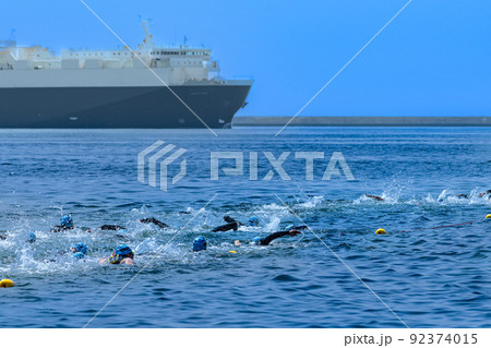 力泳するトライアスロン大会スイム競技者と貨物船 92374015