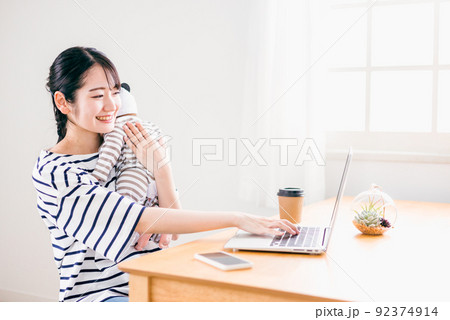家で赤ちゃんを抱っこしながらテレワークする女性(保育・世話) 家で赤ちゃんを抱っこしながらテレワークする女性(保育・世話) 92374914
