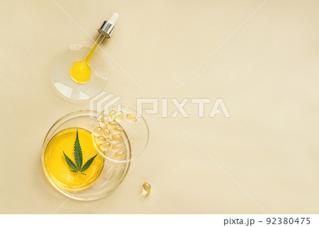 CBD oil in a pipette, THC tincture in laboratory round cups and marijuana leaves on light background CBD oil in a pipette, THC tincture in laboratory round cups and marijuana leaves on light background 92380475