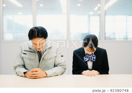 作業着を着た男性と事務スタッフの女性(お辞儀・笑顔) 作業着を着た男性と事務スタッフの女性(お辞儀・笑顔) 92380748